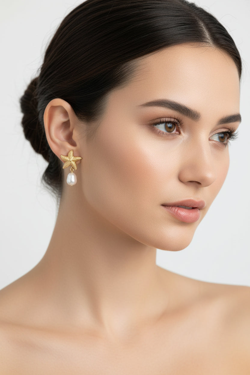 Gold starfish-shaped earrings with pearls on a textured surface