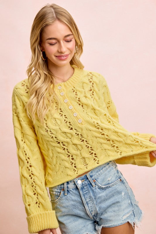 Woman wearing a yellow cable knit sweater and denim shorts on a pink background