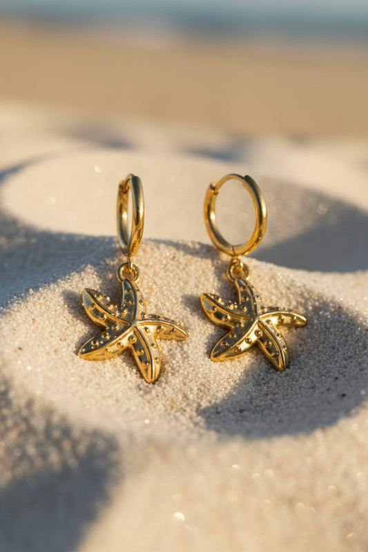 Gold starfish-shaped earrings on a textured gray surface