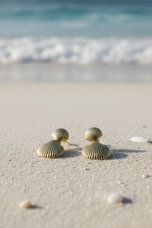 Gold shell-shaped earrings on a beige surface