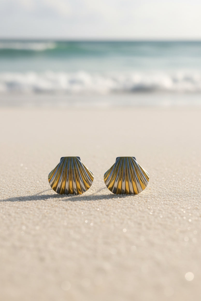 Pair of shell-shaped earrings in gold and silver on a textured beige background