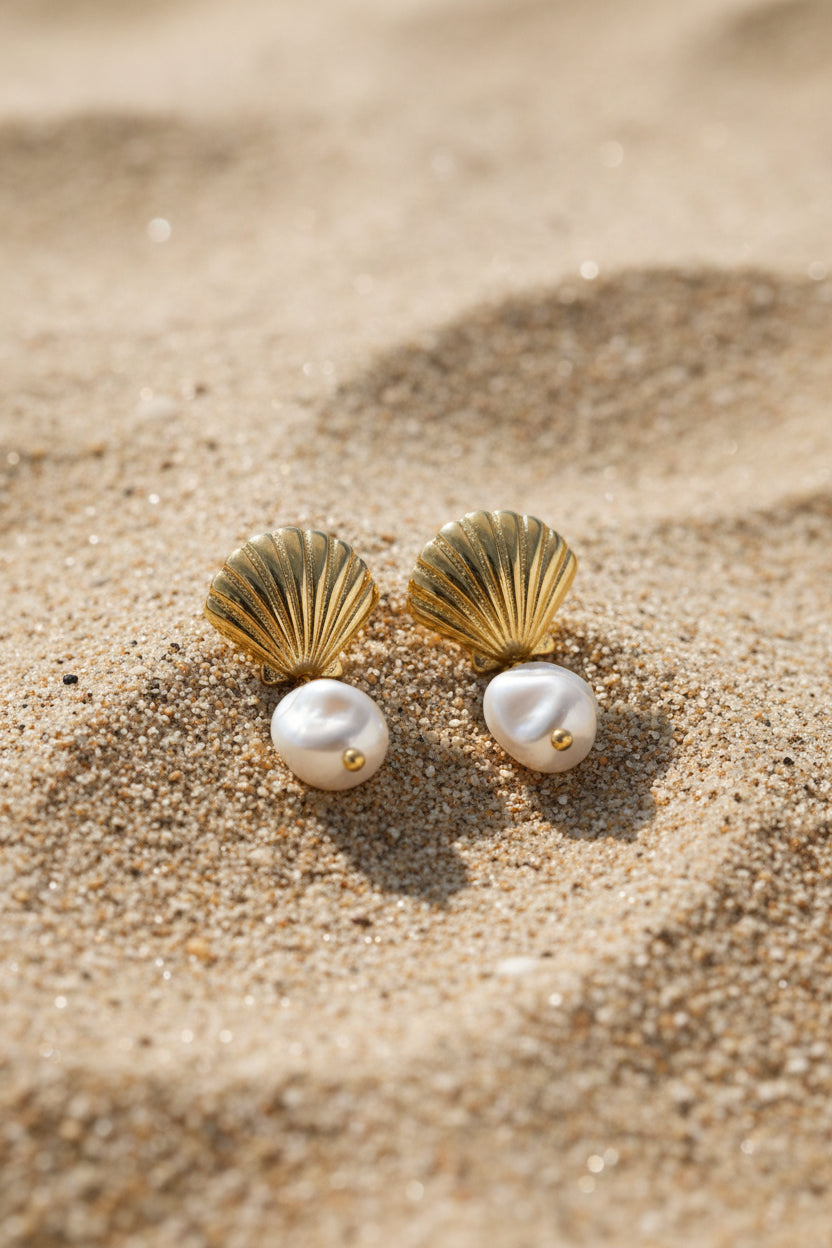 Gold earrings with pearl-like stones on a beige surface