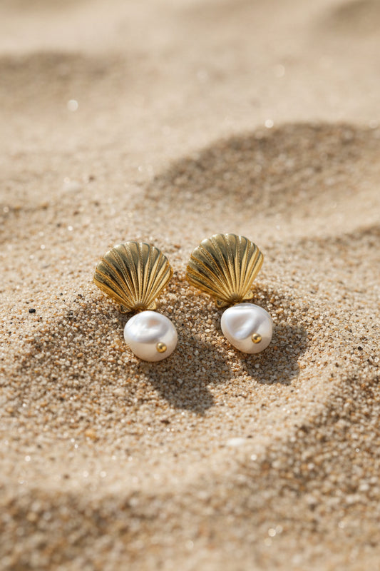 Gold earrings with pearl-like stones on a beige surface