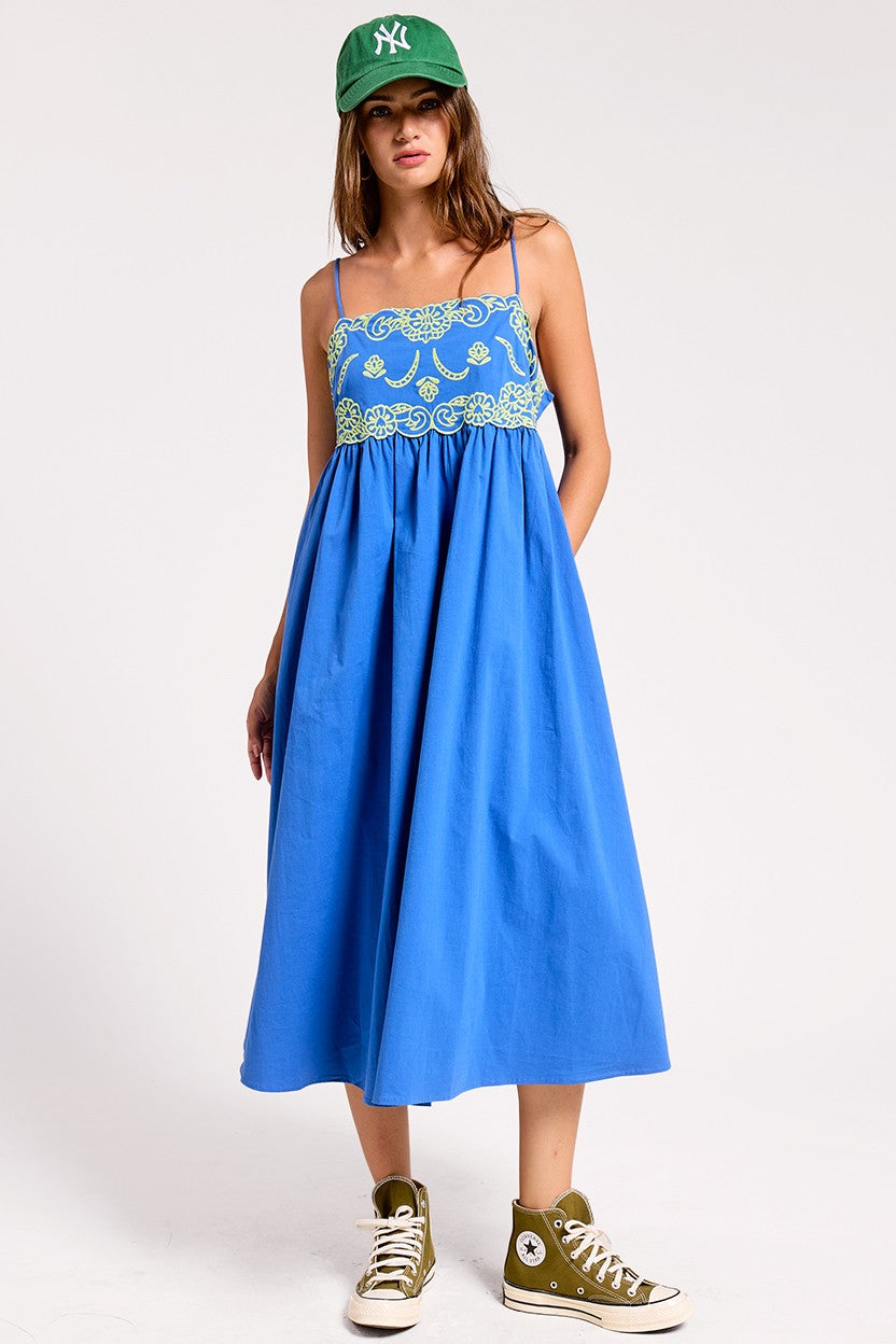 Woman wearing a blue dress with floral lace top and green cap on a white background