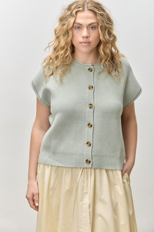 Woman wearing a light green knitted vest over a beige dress on a plain background