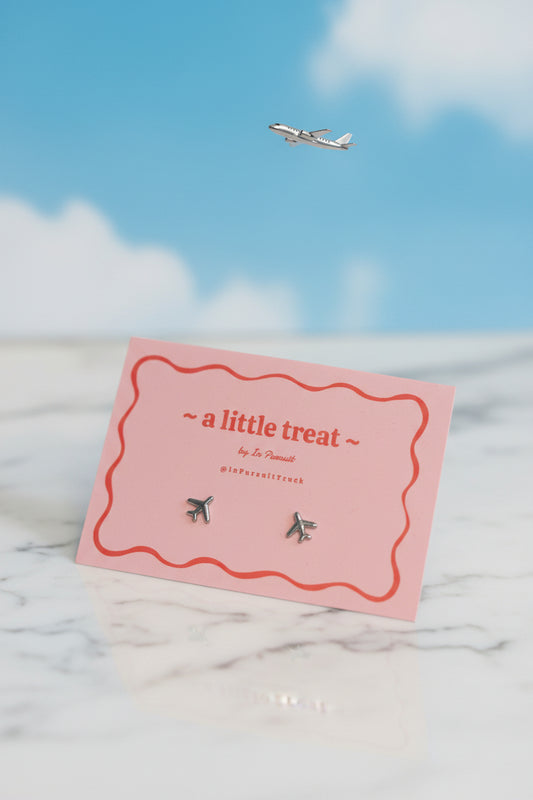 Pink card with airplane earrings on a light gray background